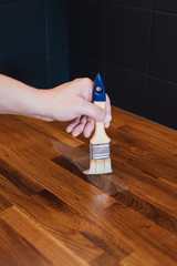 Close up of man's hand applying linseed wood treatment oil with paint brush for protection against water on wooden oak kitchen counter surface after sanding with sanding paper