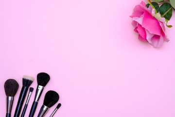 Set of makeup brushes and flower on pink colored composed background. Top view point, flat lay, space for text