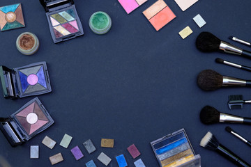 Set of make-up brushes and decorative cosmetics on dark blue colored composed background. Top view point, flat lay, space for text.