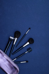 Set of makeup brushes with cosmetics bag on dark blue colored composed background. Top view point, flat lay