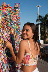 Girl tying colored ribbons on the grid in front of Bonfim church in Salvador, Bahia, Brazil