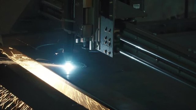 Industrial laser cutter with sparks. Clip. The programmed robot head cuts with the aid of a huge sheet of metal temperature. Close-up