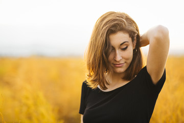 Young beautiful girl in the field. She wears a black T-shirt and jeans. Yellow background.