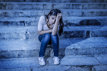 expressionist edited portrait of young sad and depressed woman or teen girl sitting lonely at street staircase looking desperate and suffering