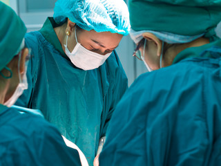 Portrait of Asian female doctor or surgeon doing operation in operating room at hospital for surgical treatment of acute bleeding patient in emergency condition 