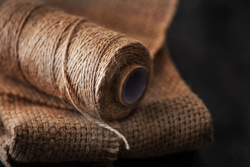 Natural jute twine roll, burlap on black background. Supplies and tools for handmade hobby leisure - obrazy, fototapety, plakaty