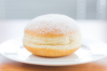 Traditional Polish Paczek with powdered sugar on white plate.