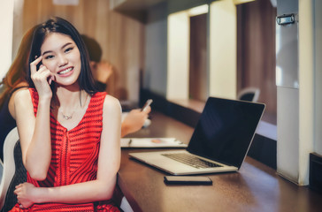 Beautiful Asian female businesswoman wearing a red dress with a laptop and smiling bright and confident in the work.