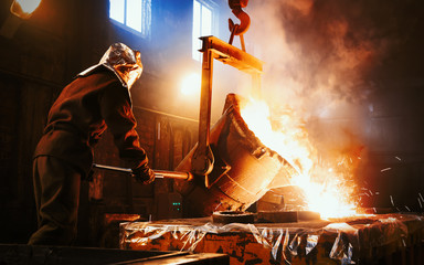 Workers operates at the metallurgical plant. The liquid metal is poured into molds. Worker...