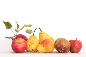 Three ripe yellow skinned pears red apples, one pomegranate, fresh organic beautiful studio shot with stems and green leaves