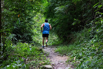 Obraz premium Athletic runner running on tropical forest trail, dramatic tone