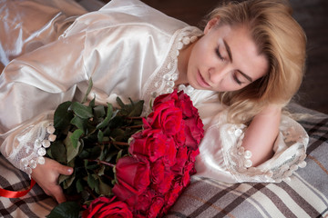 Beautiful young woman with a bouquet of roses on the bed