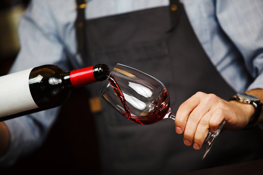 Man pouring wine into wineglass, male hand holding bottle