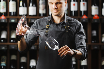 Bartender pours red wine in glass from big transparent vessel