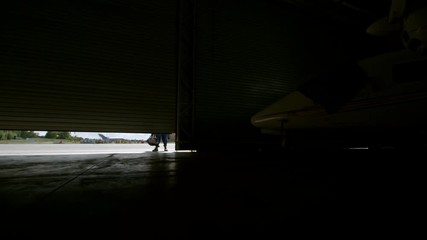 Zoom in of smiling female aircraft mechanic in uniform opening folding door and walking into hangar - Powered by Adobe