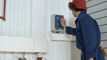 Female aircraft mechanic in blue uniform walking in hangar and pushing the button while opening folding door - Powered by Adobe
