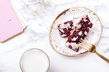 Homemade berries sponge cake slices served on white plate, cup of milk and white flowers on grey marble table. Summer breakfast. Selective focus 