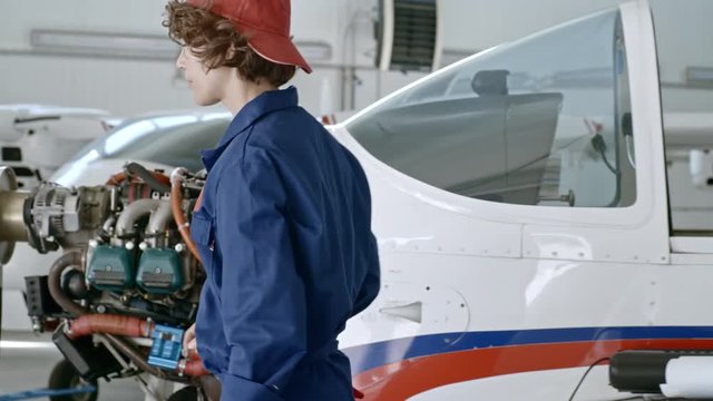 PAN of female aircraft maintenance engineer using instruments while repairing broken engine of jet airplane in hangar