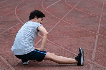 Healthy young Asian runner man warming up before run on track in the stadium