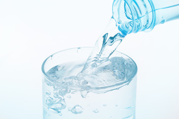 Pouring water from bottle into glass on white background.