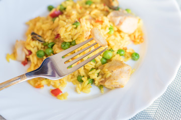 paella with chicken and seafood on white plate. Spanish dish served on table. Shrimp on a fork