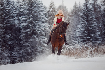 Fototapeta na wymiar Close-up of girl rider riding gallop on horse through winter forest. Racing in snow.