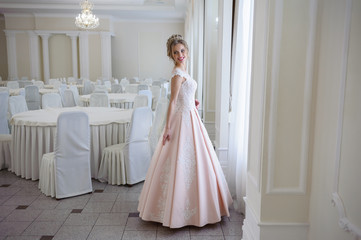 Fototapeta na wymiar A beautiful woman in a pink wedding dress in a big festive hall