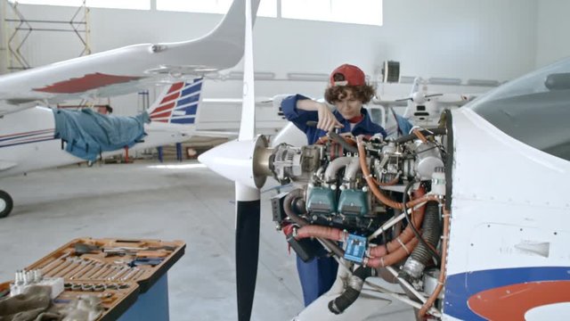 Zoom in of concentrated female maintenance mechanic fixing engine of jet airplane with instrument while working in hangar