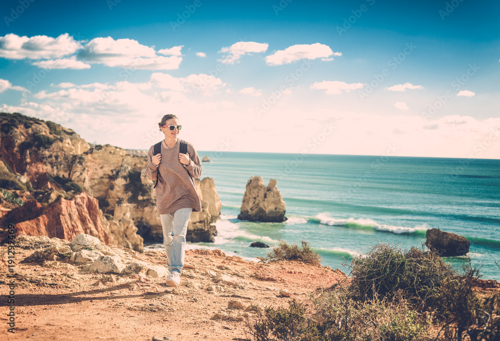 Wall mural a traveler with a backpack walks along the rocky coast of the ocean, admiring the incredible scenery