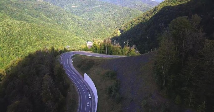 Training of professional race cyclists uphill on a mountain serpentine with an escort vehicle. Aerial follow view