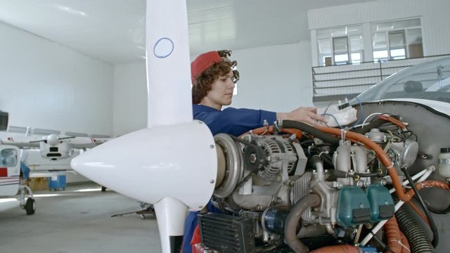 Professional female maintenance mechanic attaching testing device to airplane engine in hangar