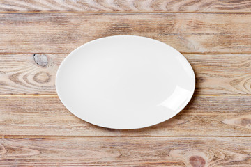 Empty white plate on wooden table. top view