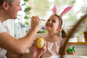 A father and daughter celebrating Easter, painting eggs with brush. Happy family smiling and...
