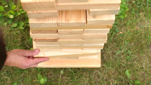 High tower of wooden blocks in the game jenga. Man plays jenga outdoor, close-up. Man playing big jenga game in the Park, close-up.