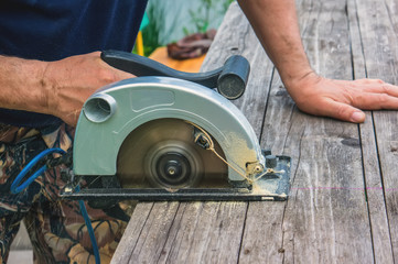A man's hand cuts a piece of plank into a Sunny day on a garden plot by marking it with a circular saw. Manual work.