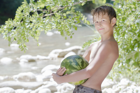 Boy in beach shade holding big green watermelon outdoors