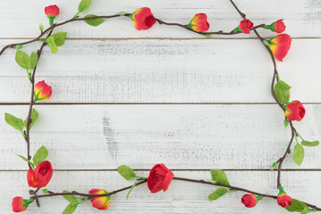 Fake red flowers with branch on white wood background with copy space