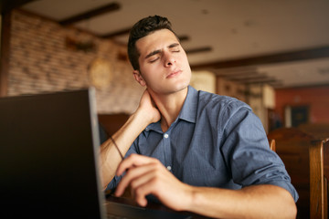 Businessman with backpain after long hours at work rubbing his neck because of ache. Overworked handsome freelancer man with scoliosis working with laptop. Health problems theme.