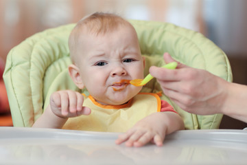 Cute baby boy refusing to eat food from spoon with face dirty of vegetable puree.