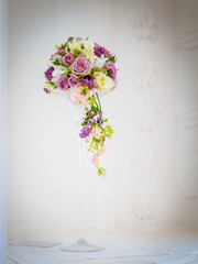The bridal bouquet with pink and white roses on the table in a tall glass vase