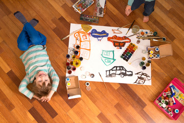 Happy cheerful children drawing with brush in paper using a lot of painting tools.   Top view.