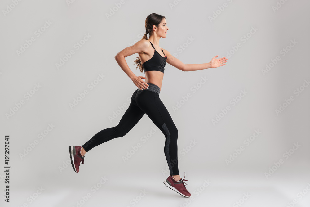 Wall mural profile picture of energetic caucasian female in sportswear running, isolated along gray background