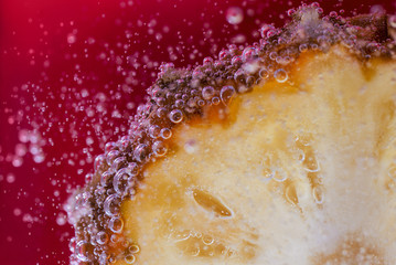 Naklejka na ściany i meble A slice of pineapple is in soda water on the red background. 