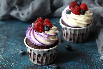 Homemade chocolate cupcakes with cream cheese cap and berries on a dark blue background.