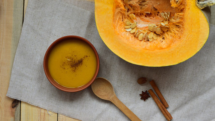 top view pumpkin pureed soup for vegetarian, healthy concept , in a clay plate, spices (cinnamon steaks, a star anise, and whole nutmeg), wooden spoon lay on linen cloth, pumpkin with seeds on wooden
