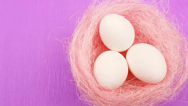 White easter eggs in pink pastel nest on purple texture background.