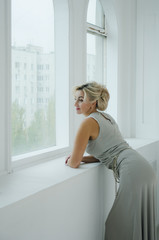 A beautiful lady of 40 years in a long evening dress looks out the window.