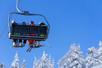 Skiers on a ski lift in the mountain on the background of a clear blue sky with copy space.
