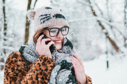 Attractive girl wears glasses talking by smartphone in winter snowy park