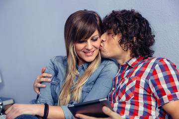 Closeup of handsome man kissing to young beautiful woman and holding electronic tablet in his hand. Love and leisure time concept.